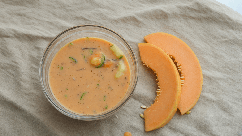 Bol de soupe orangée, avec deux tranches de melon à côté.