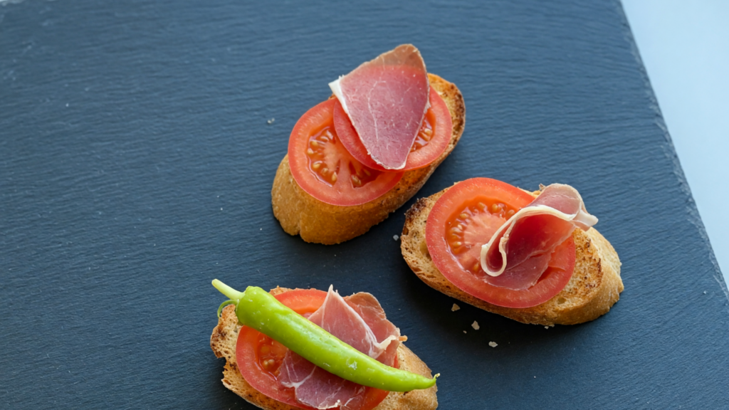Trois tartines de tomate et de jambon cru, posées sur une ardoise.