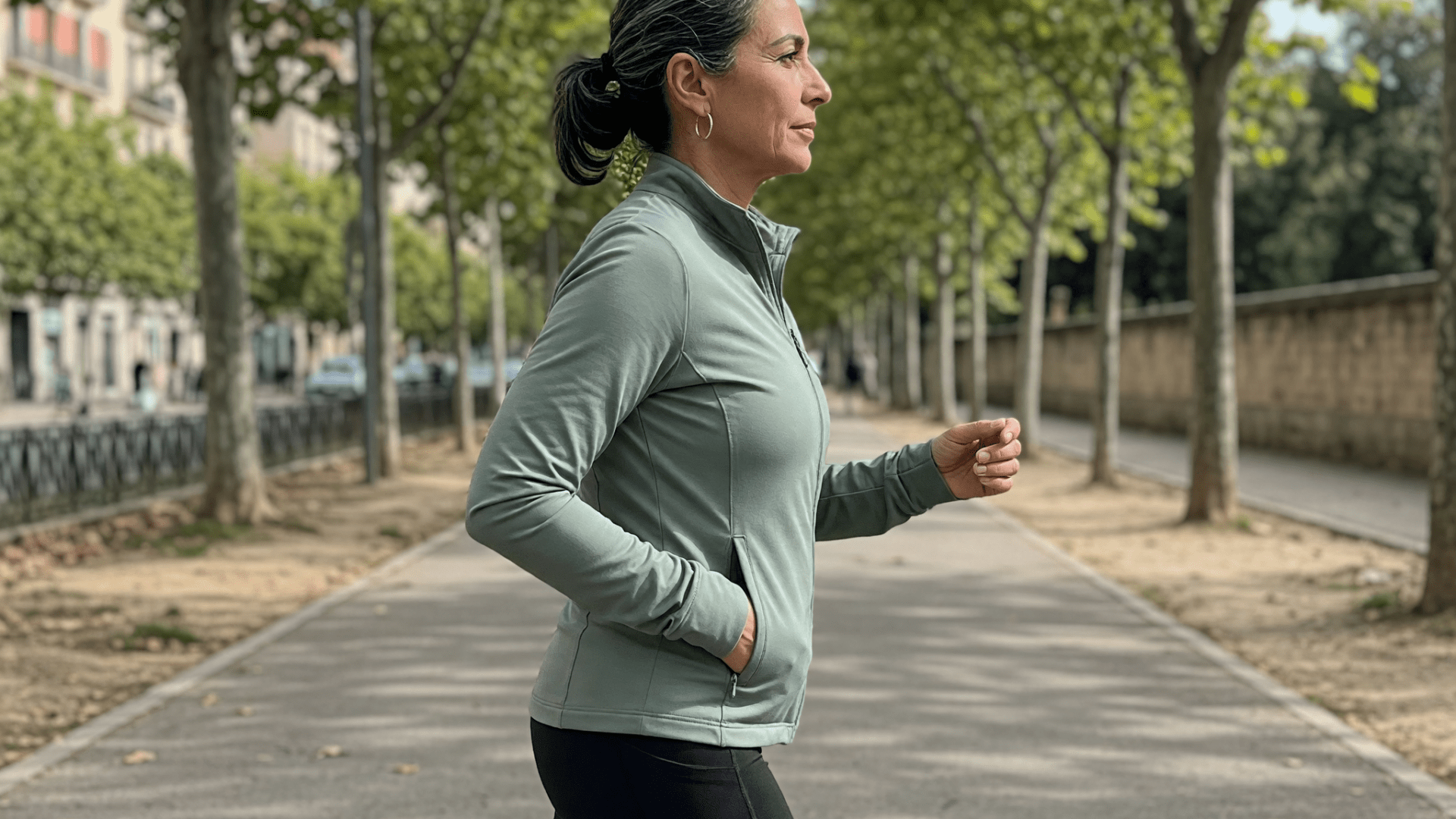 Une femme en tenue de sport marche d'un pas rapide sur une allée bordée d'arbres.