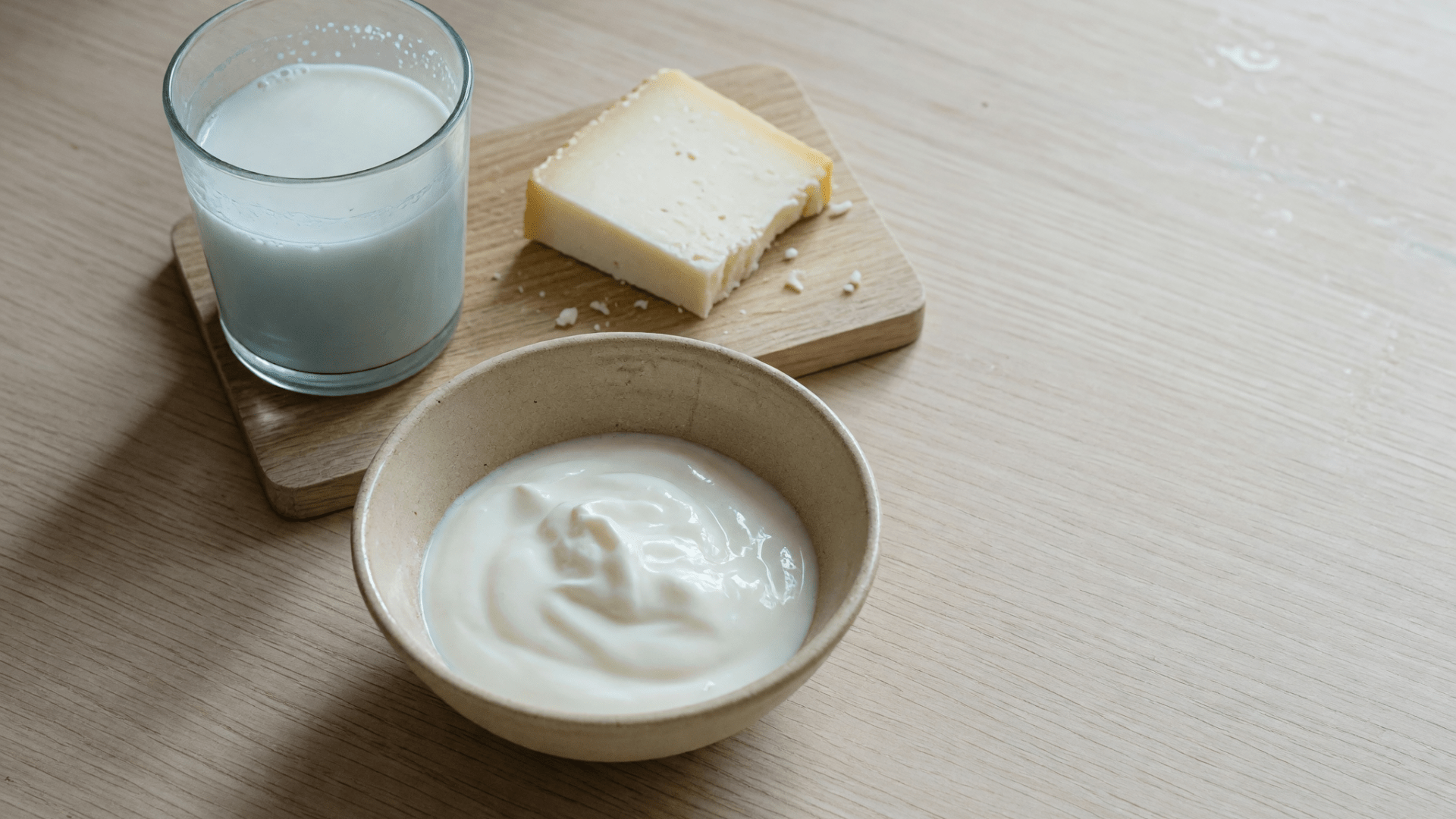 Un verre de lait, un morceau de fromage et un bol de yaourt nature sont posés sur une table en bois.