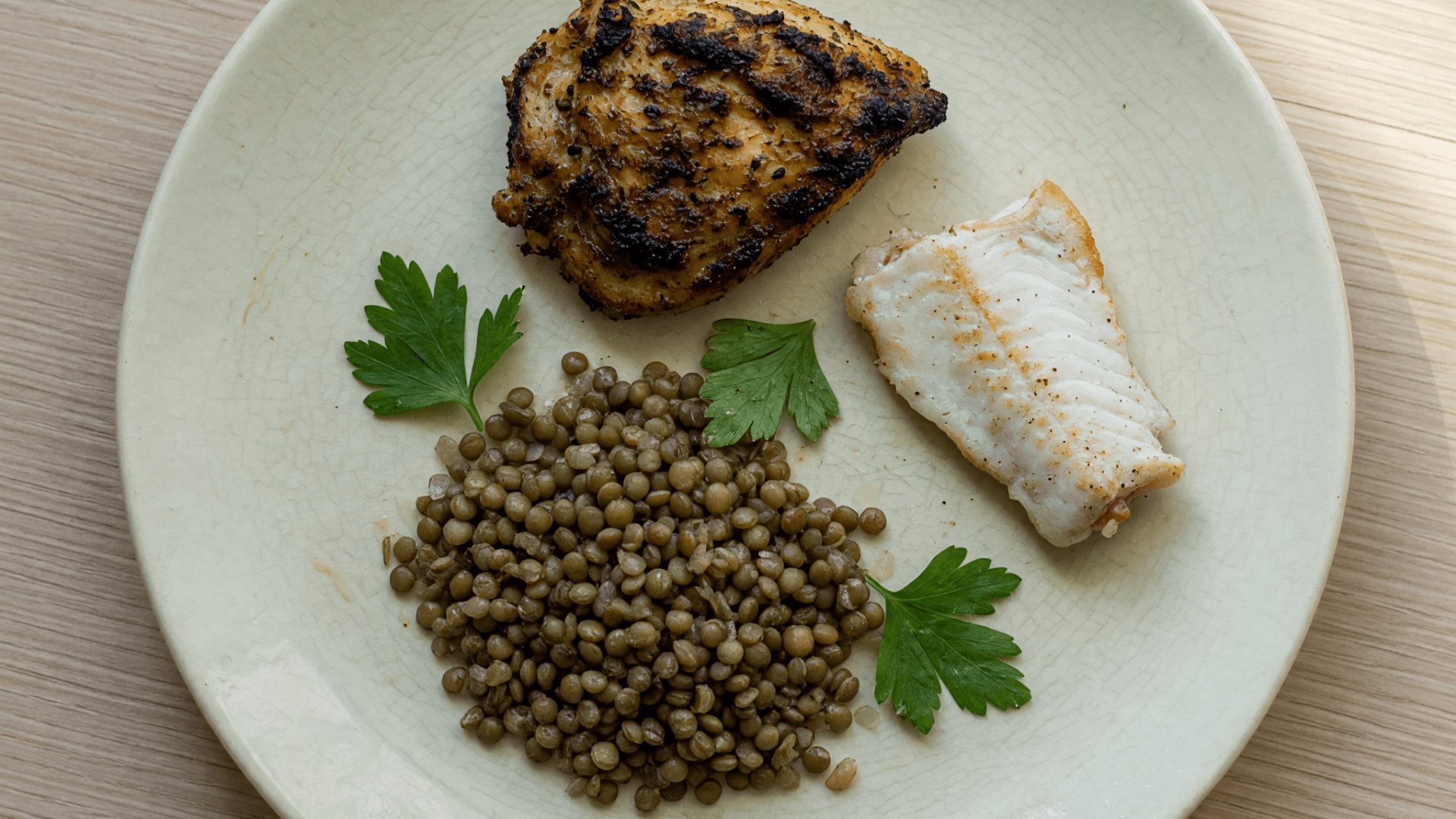 Assiette avec du poulet grillé, un filet de poisson et des lentilles.