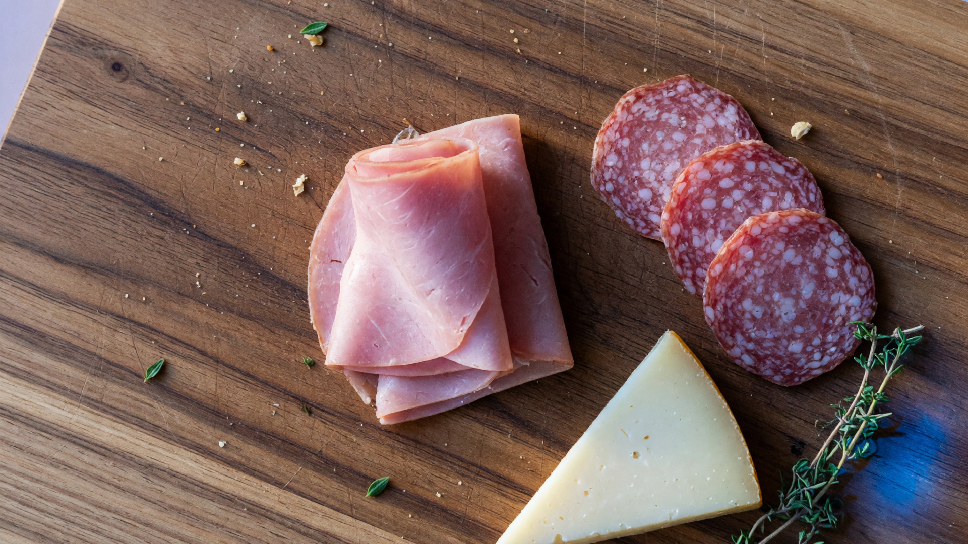 Du jambon, du salami et un morceau de fromage sur une planche.