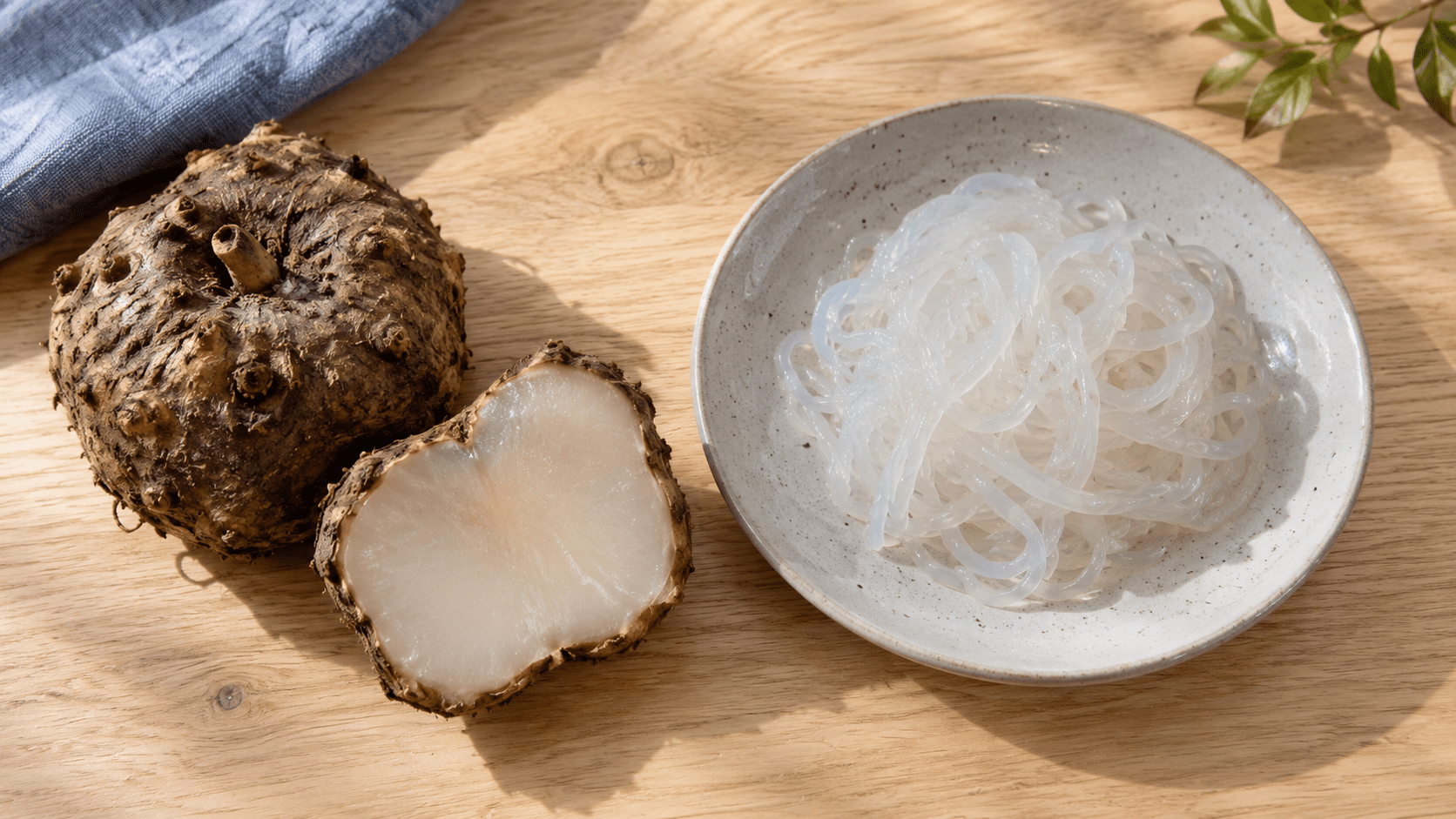 Un corme de konjac entier et une moitié, à côté d’un bol de nouilles translucides.