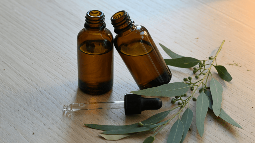 Deux flacons d'ambre ouverts, un compte-gouttes posé devant, et des feuilles d'eucalyptus.